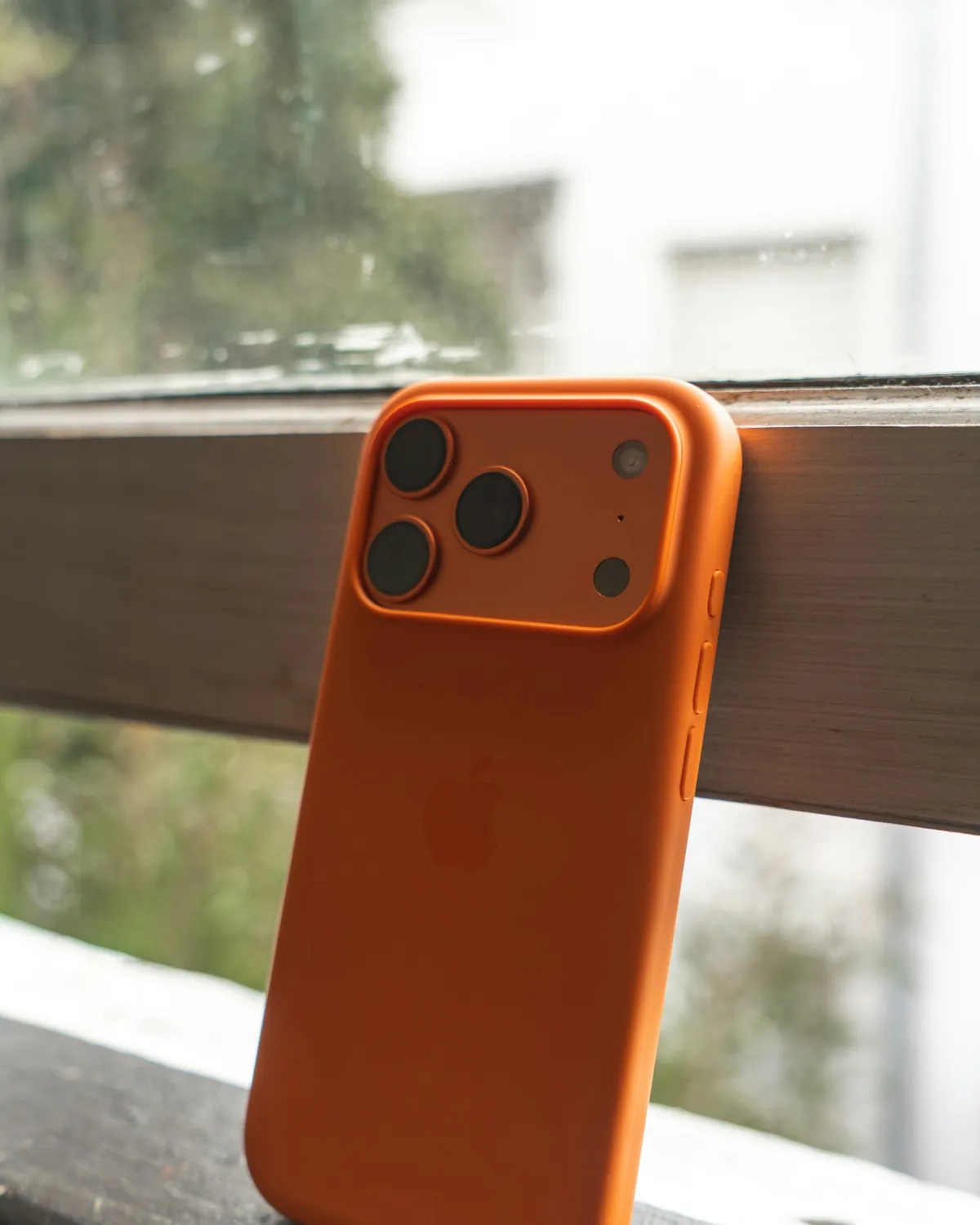iPhone con funda de silicona naranja apoyado en el marco de una ventana